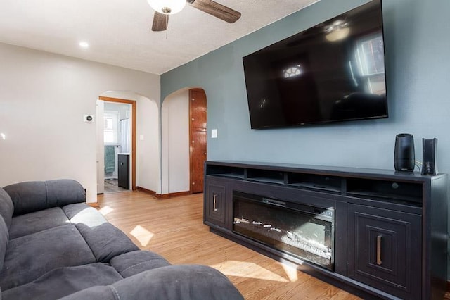 living room featuring baseboards, arched walkways, light wood-style floors, and a ceiling fan