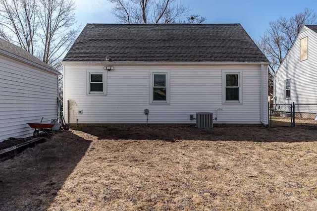 rear view of house with cooling unit, roof with shingles, and fence