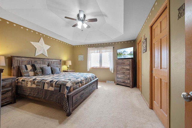 bedroom featuring a ceiling fan, baseboards, visible vents, a tray ceiling, and light carpet