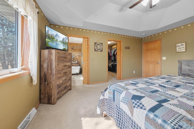 bedroom featuring visible vents, light carpet, a tray ceiling, baseboards, and a spacious closet