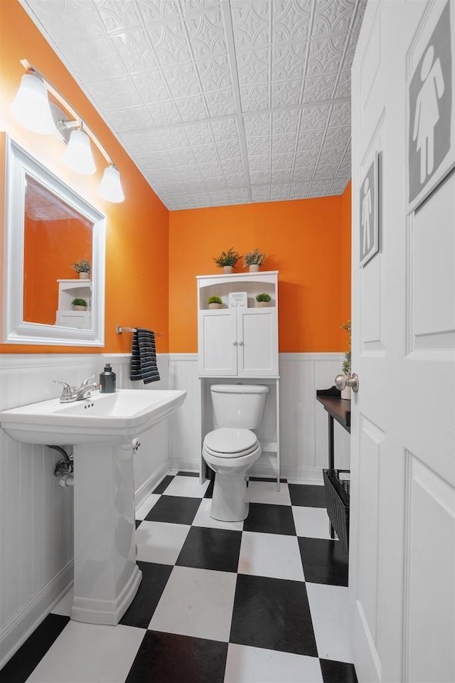 half bath featuring tile patterned floors, a wainscoted wall, and toilet