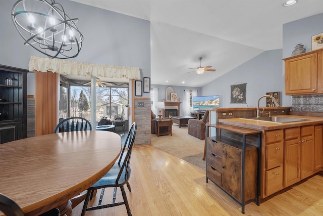 dining area featuring a glass covered fireplace, ceiling fan with notable chandelier, light wood-type flooring, and lofted ceiling