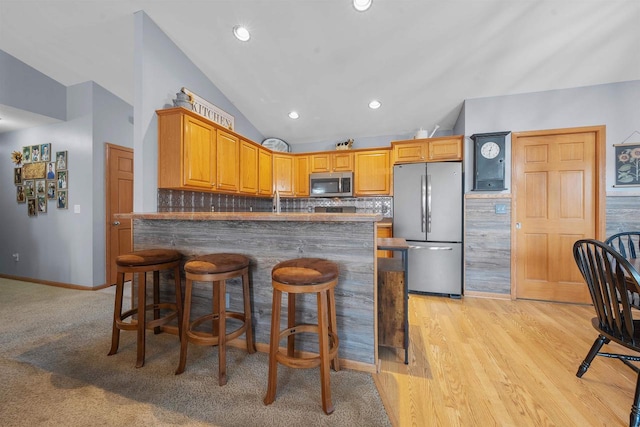 kitchen featuring backsplash, appliances with stainless steel finishes, a peninsula, and vaulted ceiling