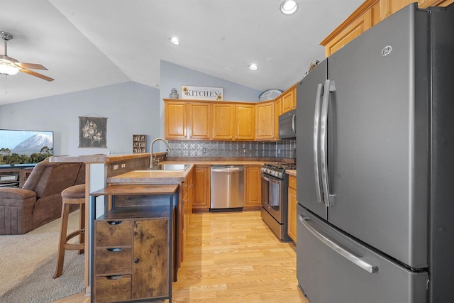 kitchen with a sink, open floor plan, stainless steel appliances, ceiling fan, and vaulted ceiling