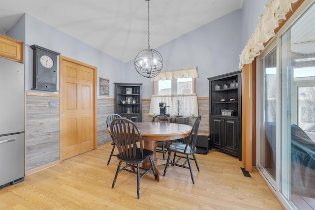 dining area with a chandelier, wainscoting, light wood finished floors, and lofted ceiling