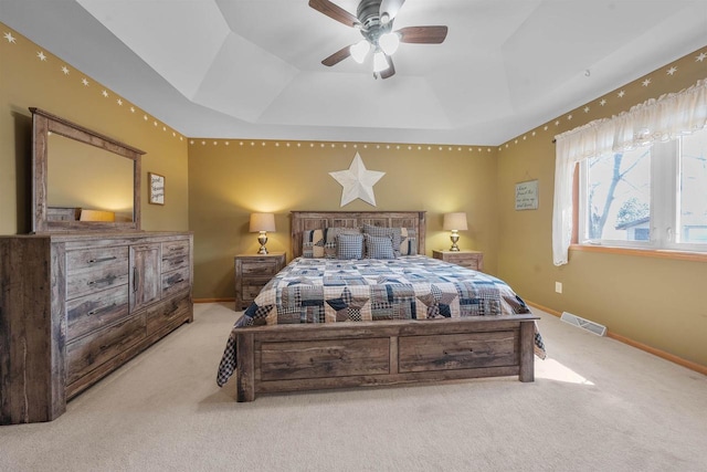 bedroom featuring visible vents, ceiling fan, baseboards, a tray ceiling, and light carpet