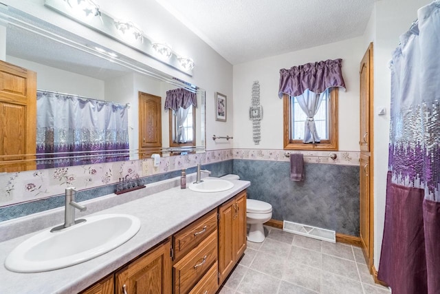 bathroom featuring a sink, visible vents, a textured ceiling, and wainscoting