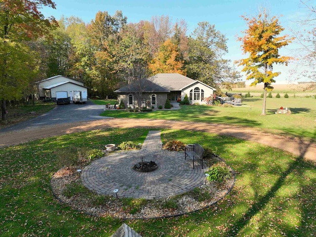 exterior space featuring curved driveway, a fire pit, a front yard, a garage, and an outdoor structure