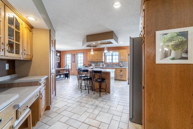 kitchen featuring a center island, glass insert cabinets, a breakfast bar area, recessed lighting, and freestanding refrigerator