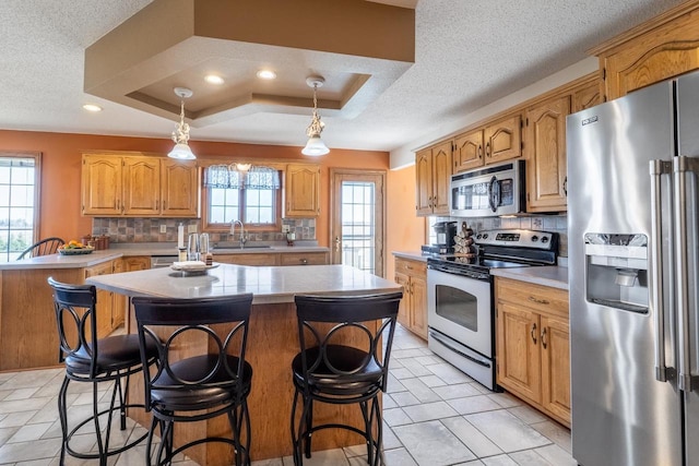 kitchen with a kitchen island, stainless steel appliances, light countertops, and a tray ceiling