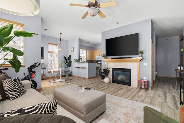 living area with baseboards, wood finished floors, ceiling fan, and a tiled fireplace