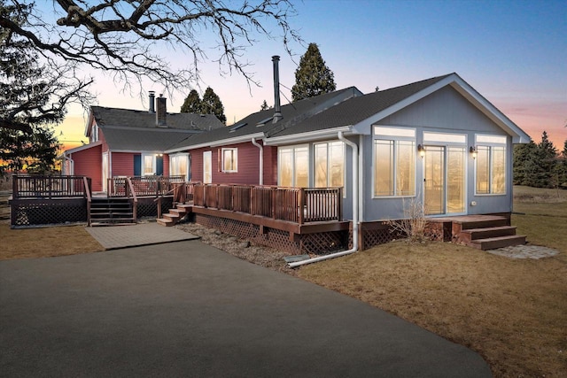 back of house at dusk with aphalt driveway, a yard, a patio, and a deck