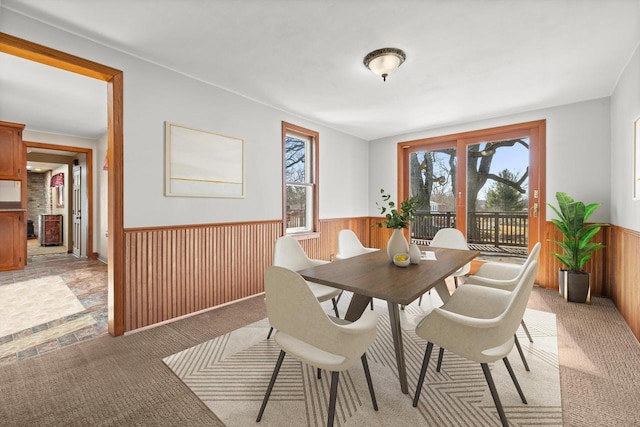 dining space featuring a wainscoted wall, light carpet, and wooden walls