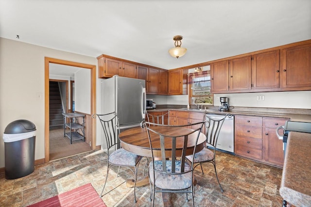 kitchen featuring brown cabinetry, stone finish floor, stainless steel appliances, and a sink