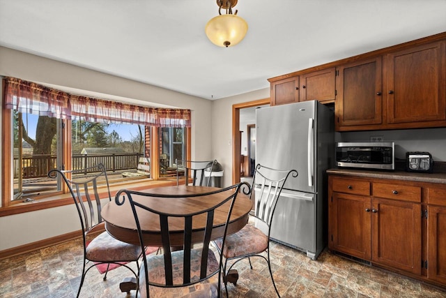 kitchen with baseboards, stainless steel appliances, stone finish floor, dark countertops, and brown cabinets