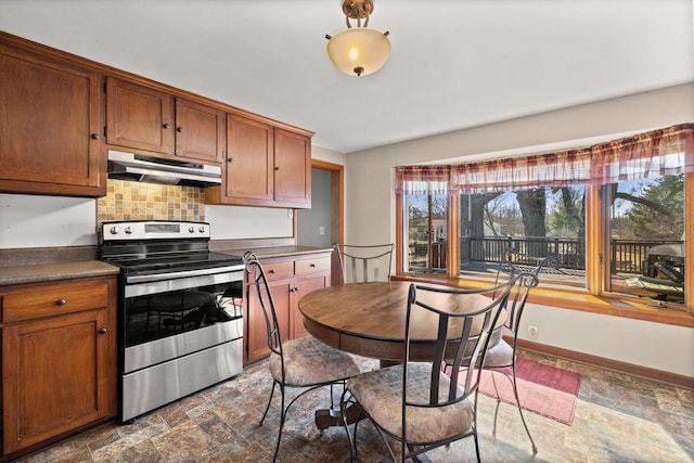 kitchen with stone finish floor, under cabinet range hood, tasteful backsplash, stainless steel range with electric cooktop, and baseboards