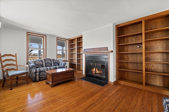 unfurnished living room featuring built in shelves, a fireplace with flush hearth, and wood-type flooring