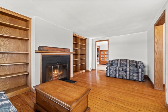 living area featuring baseboards, a fireplace with flush hearth, and hardwood / wood-style flooring