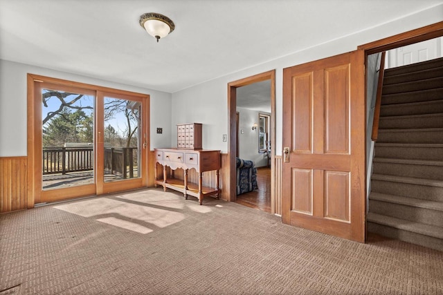 carpeted empty room with a wainscoted wall and stairs