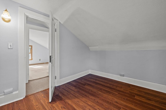 additional living space with baseboards, lofted ceiling, dark wood-type flooring, and a textured ceiling