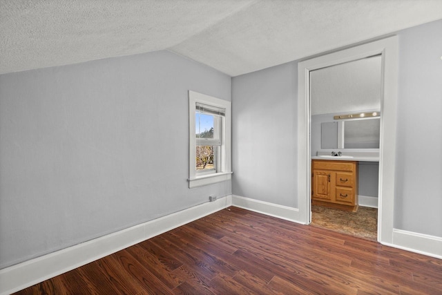 unfurnished bedroom with vaulted ceiling, dark wood-style floors, baseboards, and a textured ceiling