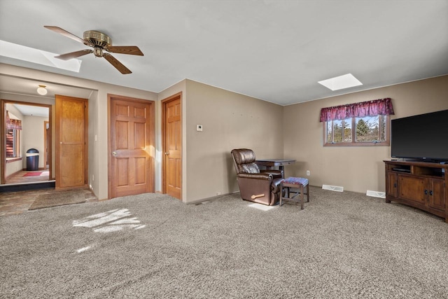 carpeted office space featuring ceiling fan, visible vents, baseboards, and a skylight