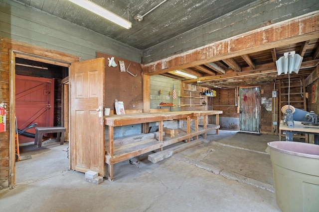 misc room with unfinished concrete floors, a workshop area, and wooden walls