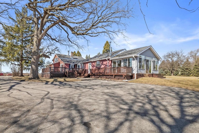 exterior space featuring aphalt driveway, a yard, a deck, and a sunroom