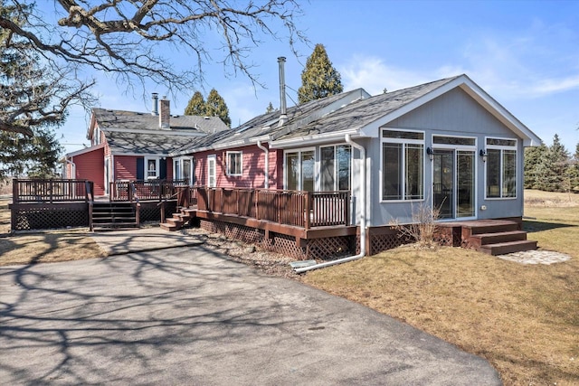 rear view of property featuring a deck, driveway, a yard, a sunroom, and a chimney