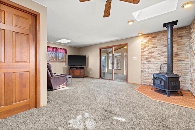 living room with carpet floors, a ceiling fan, a skylight, and a wood stove