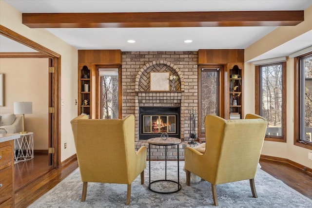 living room with a brick fireplace, baseboards, beam ceiling, recessed lighting, and wood finished floors