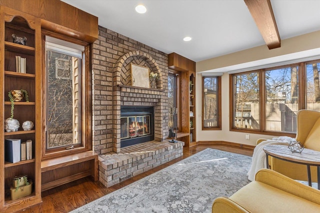 living room with a brick fireplace, baseboards, beam ceiling, recessed lighting, and wood finished floors