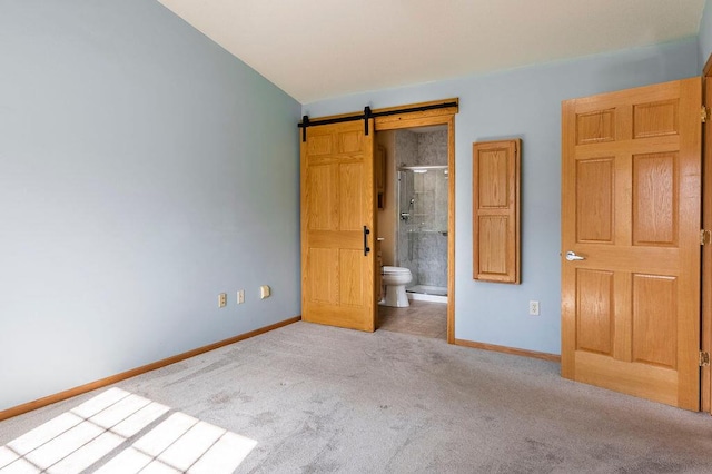 unfurnished bedroom with a barn door, carpet flooring, ensuite bathroom, and baseboards