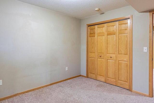 unfurnished bedroom with light carpet, a closet, a textured ceiling, and baseboards