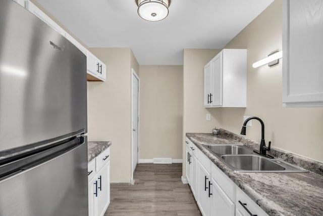 kitchen with baseboards, freestanding refrigerator, a sink, white cabinets, and light wood-style floors