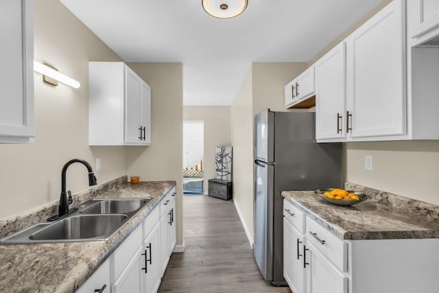 kitchen with baseboards, freestanding refrigerator, a sink, white cabinets, and light wood-type flooring