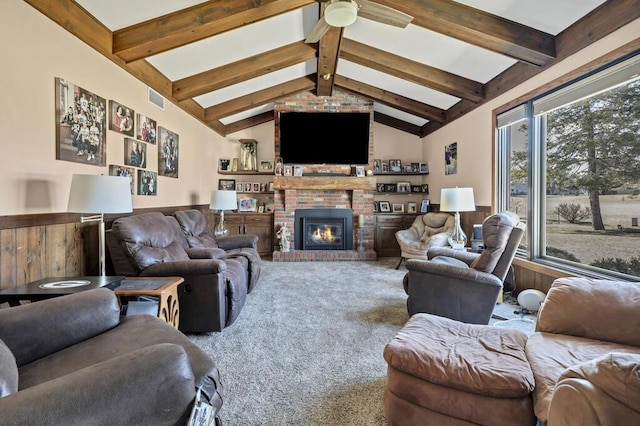 carpeted living area featuring visible vents, lofted ceiling with beams, wainscoting, a fireplace, and a ceiling fan