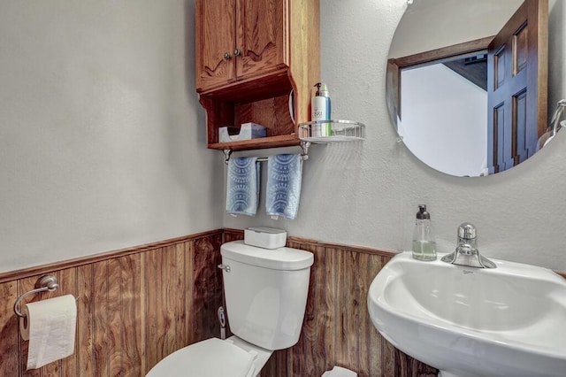 bathroom with a wainscoted wall, wood walls, toilet, and a sink