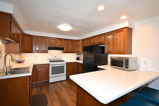 kitchen featuring stainless steel microwave, under cabinet range hood, white range with gas stovetop, freestanding refrigerator, and a sink