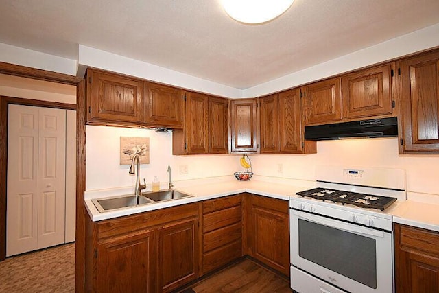 kitchen with under cabinet range hood, white gas stove, light countertops, brown cabinets, and a sink