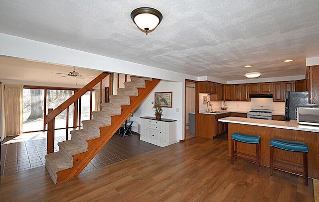 kitchen with dark wood finished floors, light countertops, under cabinet range hood, gas range, and stainless steel microwave