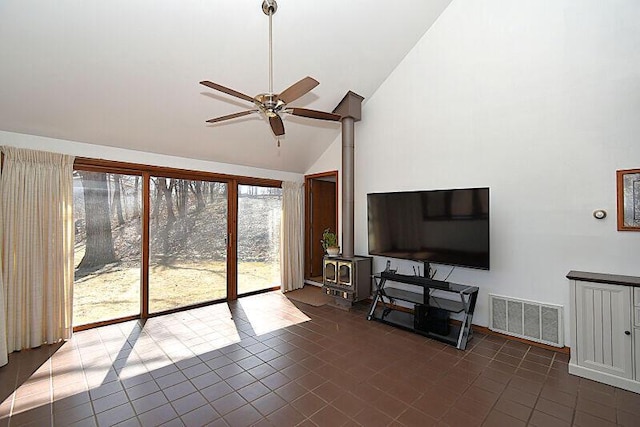 living area with visible vents, high vaulted ceiling, dark tile patterned floors, a ceiling fan, and a wood stove