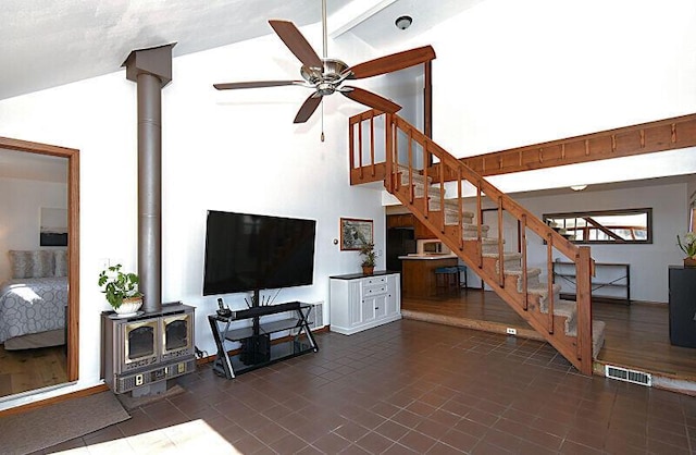 living room featuring visible vents, high vaulted ceiling, stairway, ceiling fan, and a wood stove