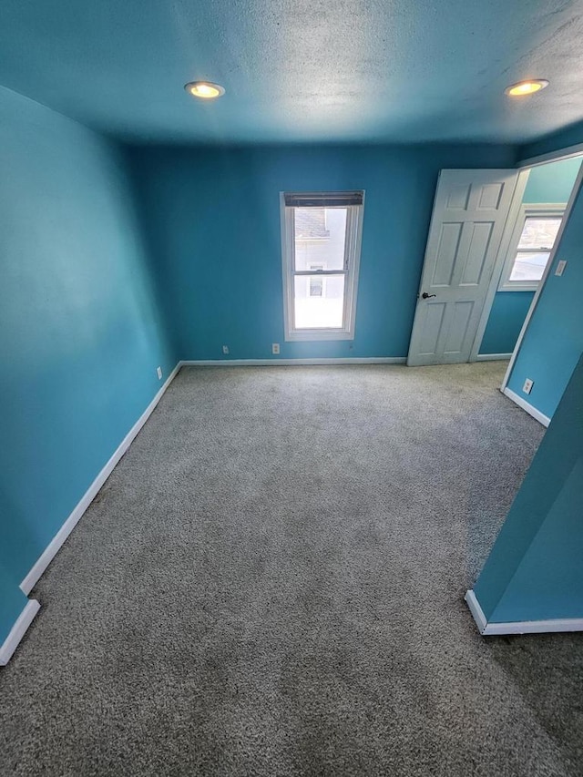 carpeted empty room featuring a textured ceiling and baseboards