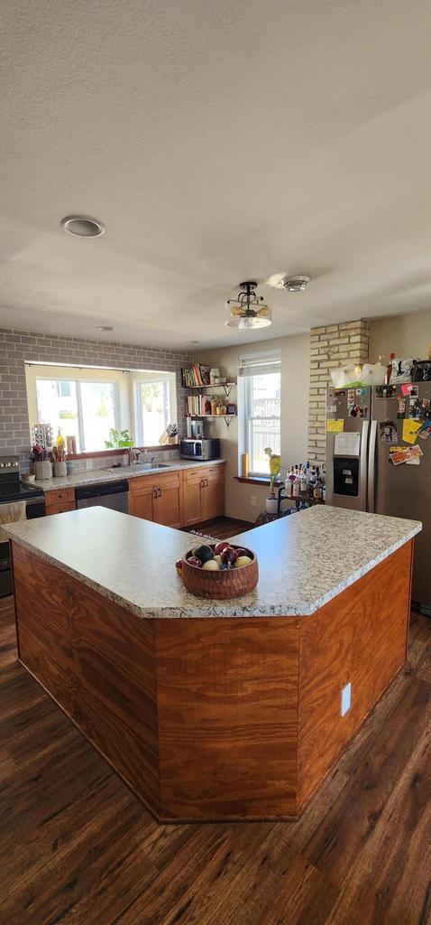 kitchen with brown cabinets, a large island, a sink, dark wood-style floors, and stainless steel appliances