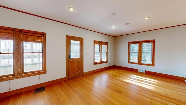 empty room featuring light wood finished floors, visible vents, baseboards, ornamental molding, and a wealth of natural light