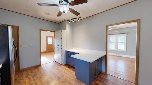 kitchen with blue cabinets, visible vents, light wood-style flooring, freestanding refrigerator, and a peninsula