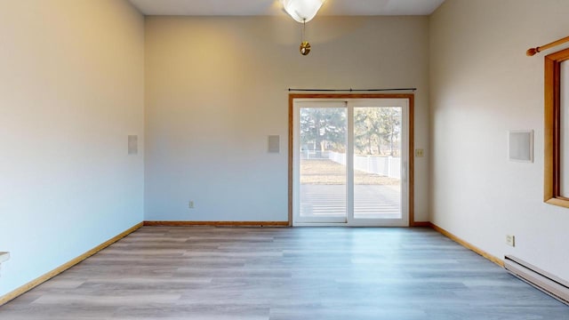 spare room featuring light wood finished floors, baseboard heating, and baseboards