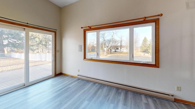 empty room featuring baseboards, plenty of natural light, baseboard heating, and wood finished floors