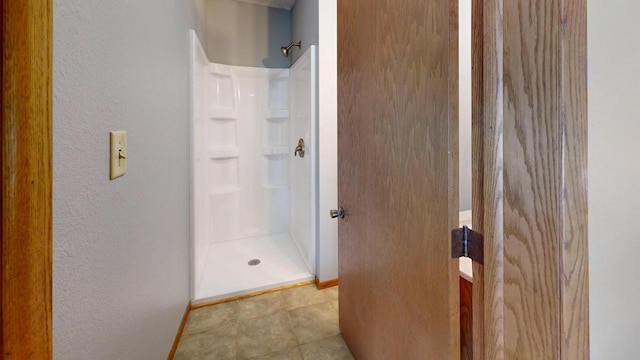 bathroom with a shower stall, a textured wall, and baseboards